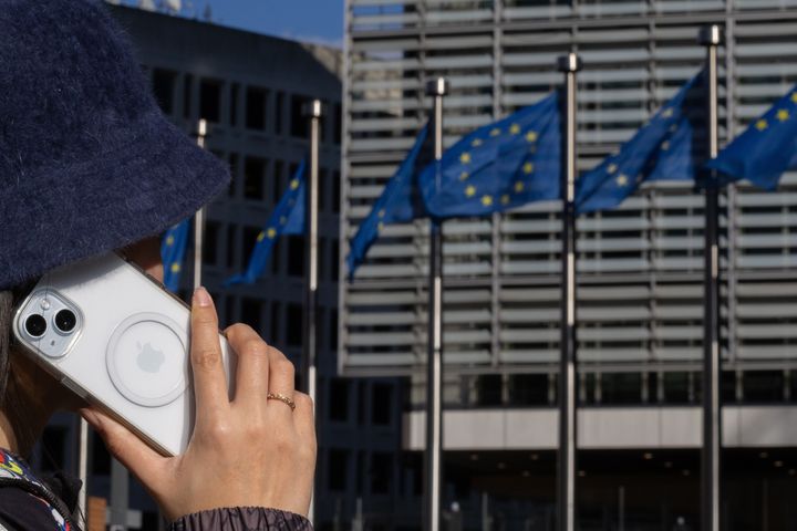 Μια γυναίκα μιλάει μέσω iPhone στο κτίριο Berlaymont, έξω από την έδρα της Ευρωπαϊκής Επιτροπής, στις Βρυξέλλες, στις 4 Μαρτίου 2024. Ήδη, η Ευρωπαϊκή Ένωση έχει επιβάλει στον τεχνολογικό γίγαντα της Apple πρόστιμα άνω των 1,8 δισεκατομμυρίων ευρώ για εικαζόμενες παραβιάσεις της αντιμονοπωλιακής νομοθεσίας. (Photo by Meng Dingbo/Xinhua via Getty Images)