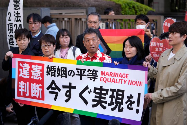 One of the plaintiffs, in a red and white shirt, center, speaks in front of media members by the main entrance of the Tokyo district court after hearing the ruling regarding LGBTQ+ marriage rights, in Tokyo, on March 14, 2024. The banner reads: 