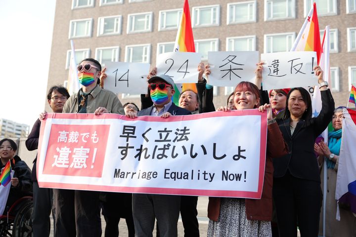 同性婚訴訟の札幌高裁判決を受け、「高裁でも違憲」などと書かれた紙を掲げる原告ら