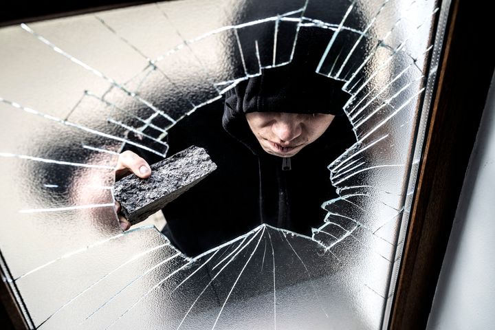 Young thug criminal smashing window with brick recognisable