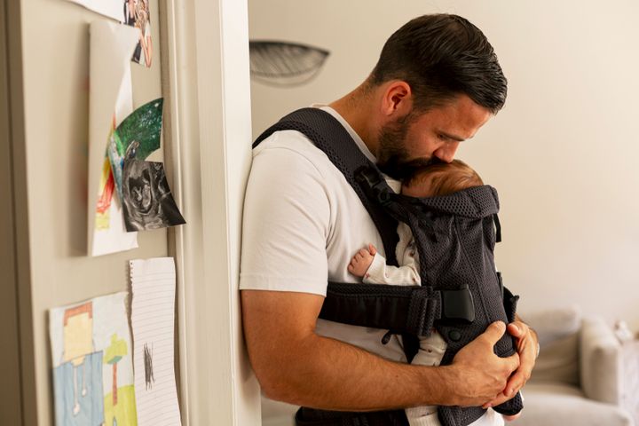 Mature father kissing baby in carrier at home