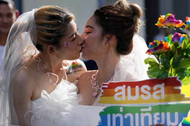 Δύο γυναίκες φιλιούνται ενώ κρατούν μια αφίσα για την υποστήριξη της ισότητας των γάμων, κατά τη διάρκεια μιας παρέλασης υπερηφάνειας στην Μπανγκόκ της Ταϊλάνδης, στις 4 Ιουνίου 2023.