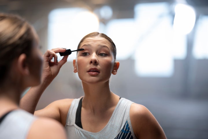 Gymnast young woman applying eyelash makeup while looking at mirror.