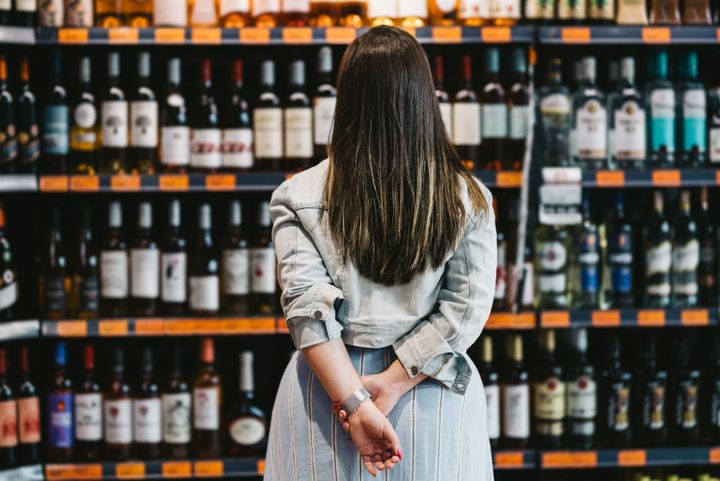 Rear view of a woman customer looking at a rack of wine in supermarket