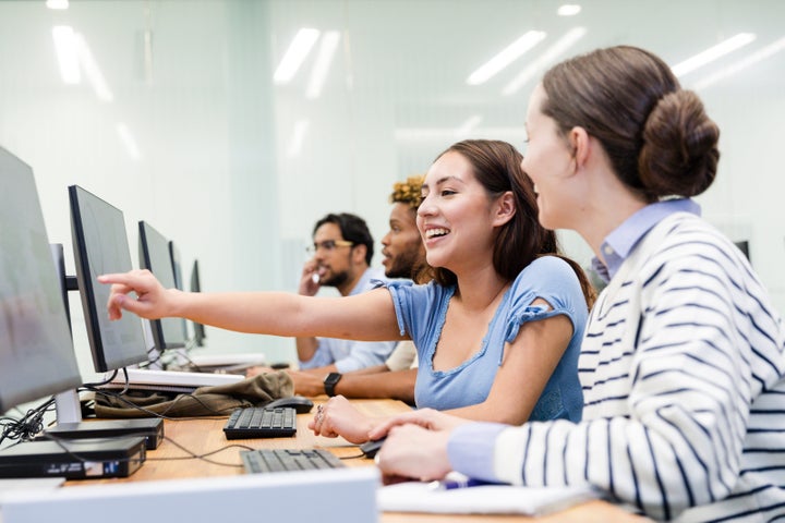 The two young adult female students work together in the computer lab on their project.