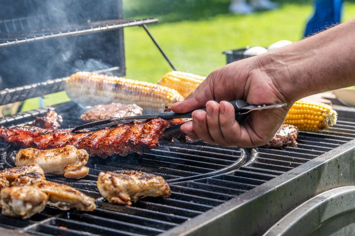 Close-up of man using tongs to take meat off on hot barbecue grill.