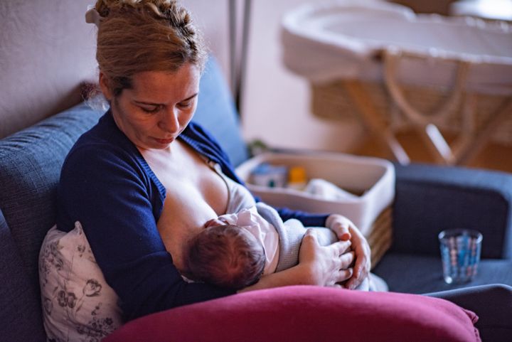 Mother breastfeeding her baby boy in arms, sitting on bed.