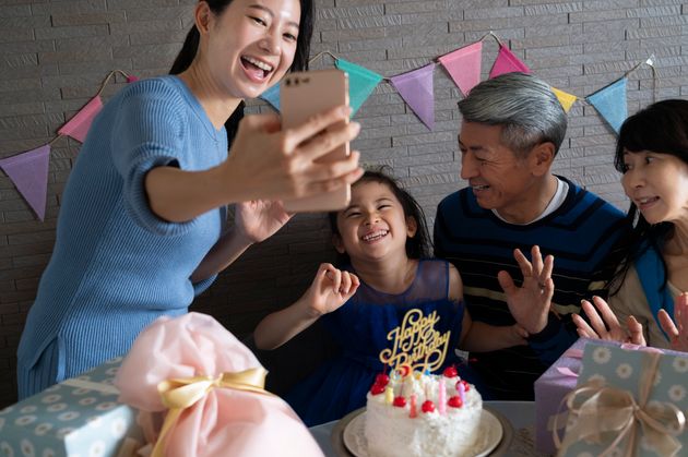 A mother uses a smartphone to take a selfie of her birthday daughter and grandparents.
