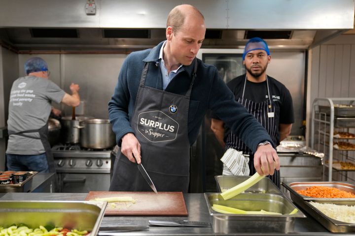 The Prince of Wales speaks with head chef Mario Confait as he cuts celery while helping to make a bolognese sauce during a visit to Surplus to Supper, a charity in southeast England.