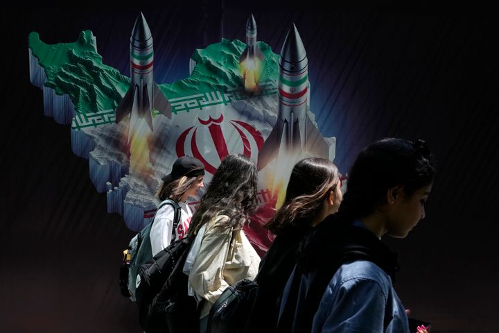 Iranian women without wearing their mandatory Islamic headscarf walk past a banner showing missiles being launched from Iranian map in northern Tehran, Iran, Friday, April 19, 2024. Iran fired air defenses at a major air base and a nuclear site near the central city of Isfahan after spotting drones early Friday morning, raising fears of a possible Israeli strike in retaliation for Tehran's unprecedented drone-and-missile assault on the country. (AP Photo/Vahid Salemi)