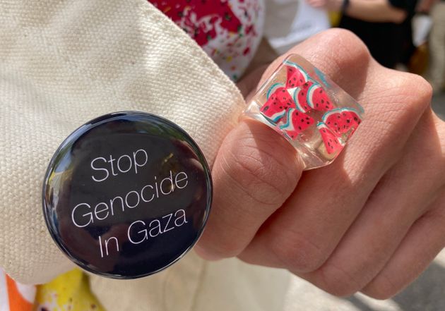 シゲさんが着用したスイカ柄の指輪と、かばんにつけた「Stop Genocide In Gaza（ガザでのジェノサイドを止めろ）」と書かれた缶バッチ