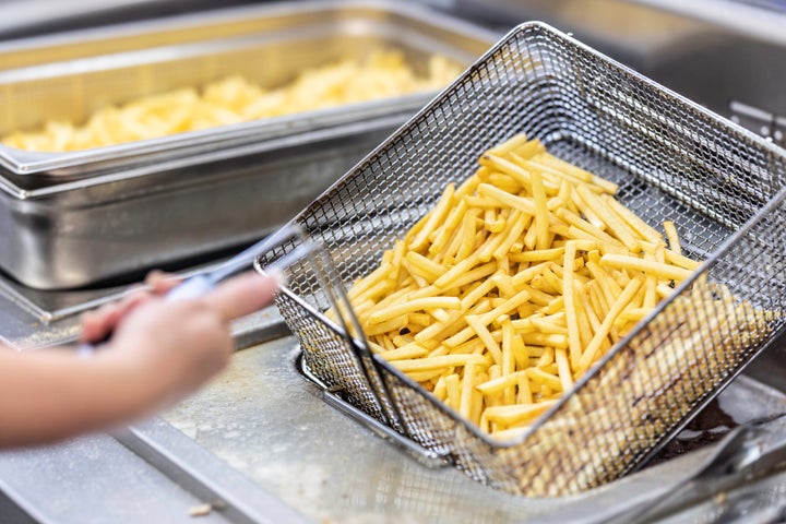 Female hands holding a frying pan with french fries at a commercial kitchen.