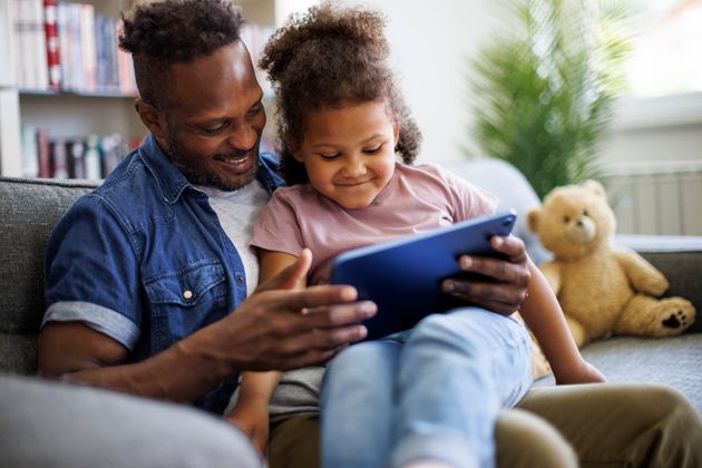 Happy African American father and adorable mixed race daughter using digital tablet in the living room at home