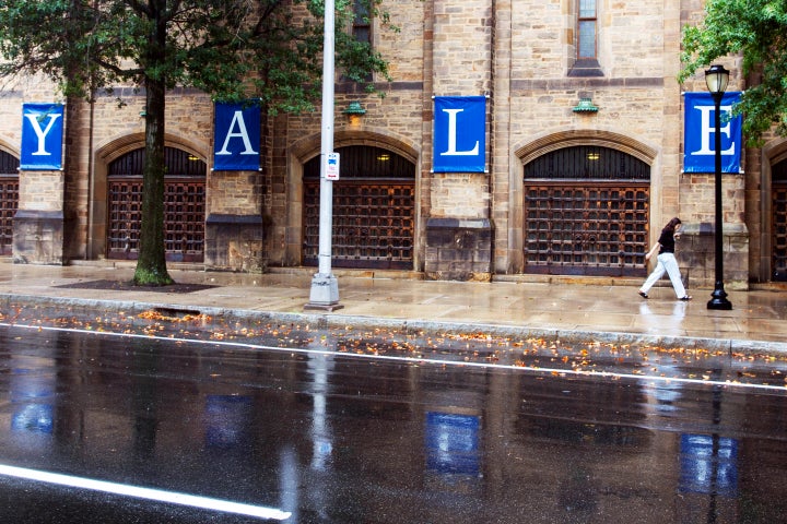 A woman walks by a Yale sign reflected in the rainwater on the Yale University campus, Aug. 22, 2021, in New Haven, Conn. Columbia University canceled in-person classes Monday, April 22, 2024 and police arrested several dozen protesters at Yale University as tensions on U.S. college campuses continue to grow over Israel's military offensive in Gaza.