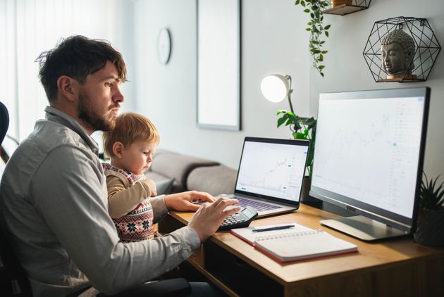 Man trading on his computer from his home office while taking care of his little son.