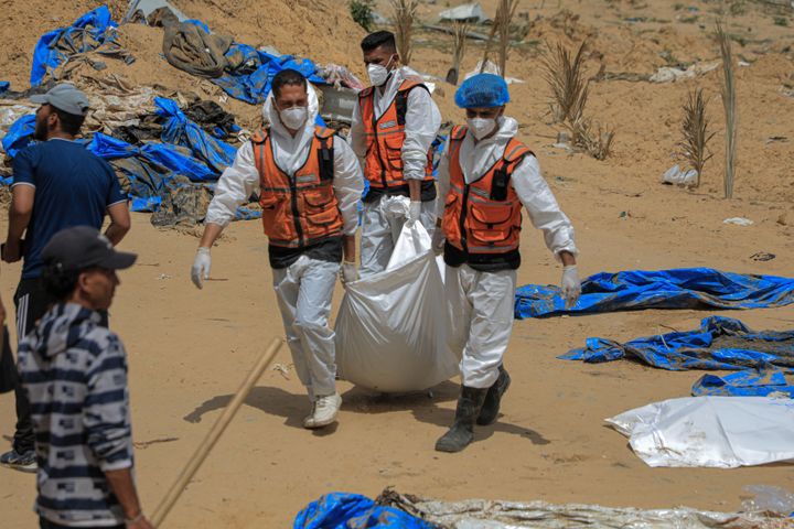 在加沙地带南部城市汗尤尼斯纳赛尔医院的乱葬坑中，工人们搬运着一具尸体。