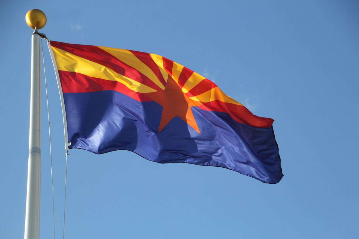 Arizona flag flies in the sky by an American flag with a bright blue sky