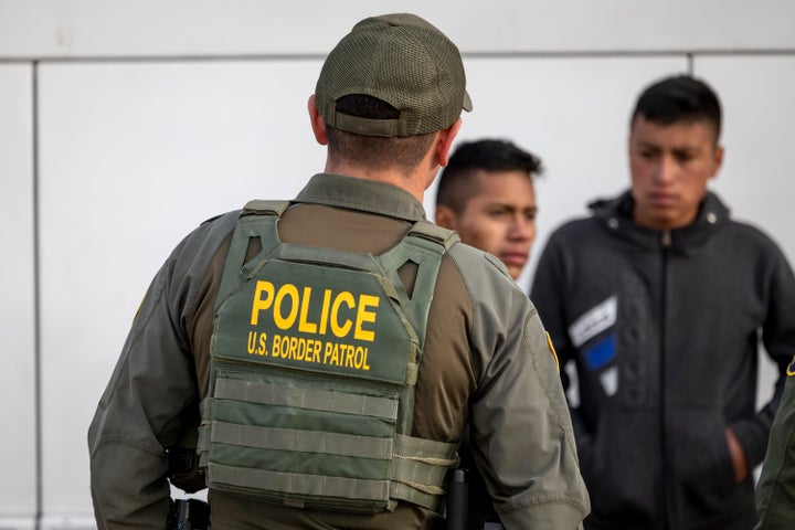 A U.S. Border Patrol agent watches on Jan. 7 as migrants prepare to board a bus after crossing the border at Eagle Pass, Texas. Documents obtained by HuffPost reveal that Border Patrol agents who used a slur for migrants also at times gloated about migrants’ misfortunes or hinted at beating them. Agents also joked about killing migrant children in their custody. 