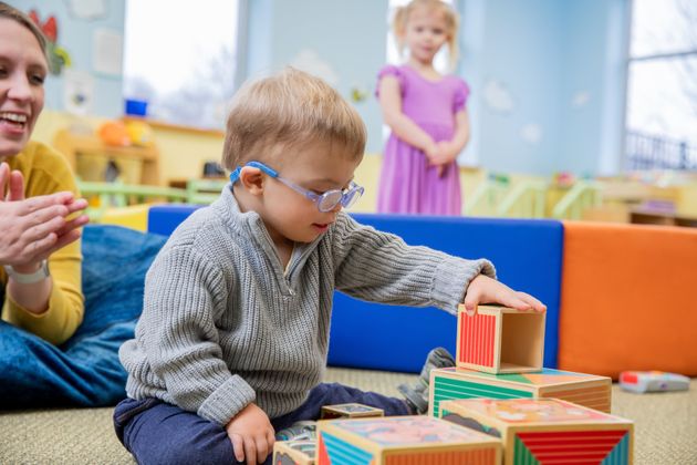 Adorable toddler boy with Down Syndrome stacks blocks in preschool classroom during occupational therapy appointment