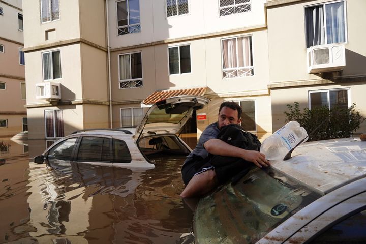 A man supports himself on a car as he tries to return to his flooded apartment building after heavy rain in Canoas, Rio Grande do Sul state, Brazil, on May 9, 2024.