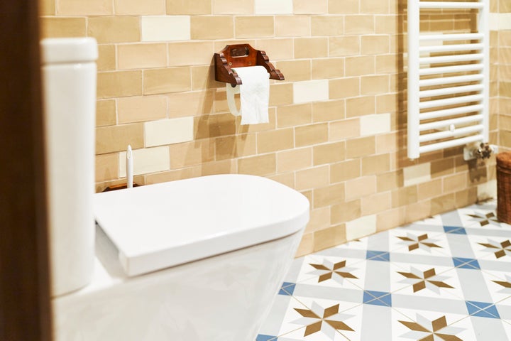 side view of a toilet in a bathroom with no people around with some paper on the wall