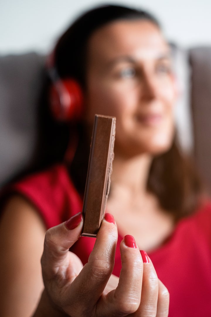 Young woman listening to music with headphones and eating a chocolate bar.