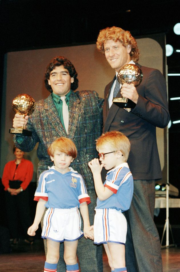 Ο αστέρας του ποδοσφαίρου της Αργεντινής Ντιέγκο Μαραντόνα, αριστερά, και ο Δυτικογερμανός τερματοφύλακας Χάραλντ Σουμάχερ κρατούν τα βραβεία που κέρδισαν στο Παγκόσμιο Κύπελλο, ενώ ποζάρουν με δύο νεαρούς ποδοσφαιριστές κατά τη διάρκεια της τελετής απονομής του Χρυσού Παπουτσιού Ποδοσφαίρου που πραγματοποιήθηκε στο Παρίσι, Γαλλία, στις 13 Νοεμβρίου 1986.
