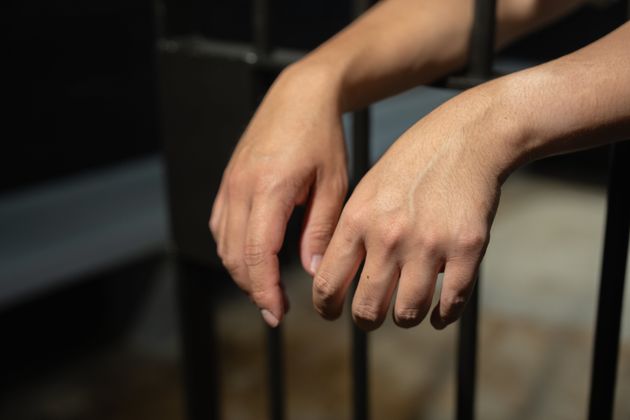 Hands of a prisoner in a cell behind bars.