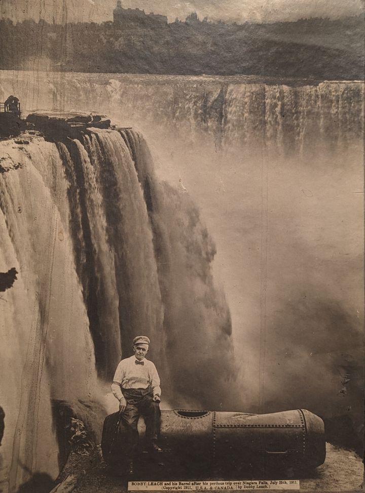 Auf dieser Fotocollage sitzt Bobby Leach nach seinem Flug über die Niagarafälle am 25. Juli 1911 auf seinem Fass.  Das Bild ist eines von mehreren Werken, die im Castellani Museum of Art der Niagara University ausgestellt sind "Rücksichtslose Leute" Eine Ausstellung, die die Reisen derjenigen beleuchtet, die es wagten, den Wasserfällen zu trotzen.