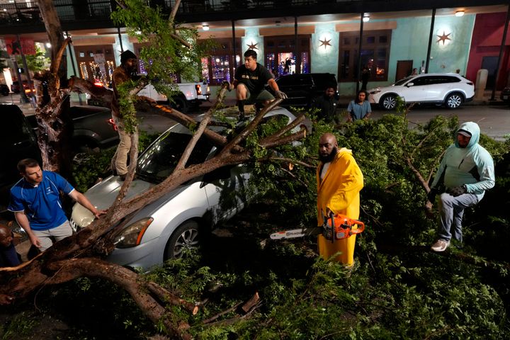 Ο ράπερ Trae tha Truth, με την κίτρινη φόρμα, κόβει κορμούς δέντρων πάνω από ένα αυτοκίνητο μετά από τη σφοδρή καταιγίδα που χτύπησε το κέντρο της πόλης, του Χιούστον την Πέμπτη, 16 Μαΐου 2024. (AP Photo/David J. Phillip)