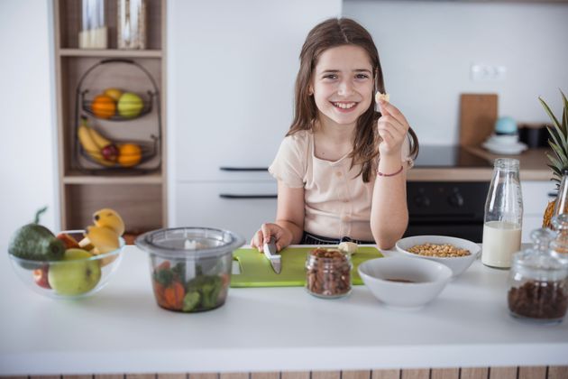 Happy young girl holding a piece of fruit when sitting in the kitchen
