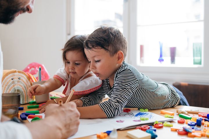 Happy siblings spending quality time with their unrecognizable father, drawing at a table.