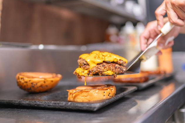 Chef assembling the buns with cheeseburgers in the restaurant kitchen, wearing a uniform