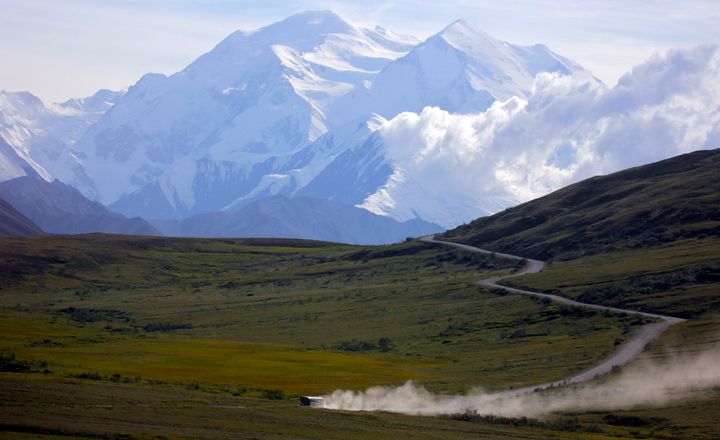 Ein Reisebus wirbelt an einem sonnigen Tag im Denali-Nationalpark in Alaska mit dem Mount Denali im Hintergrund am Donnerstag, dem 8. August 2013, Staub auf. (AP Photo/Manuel Valdes, Datei)