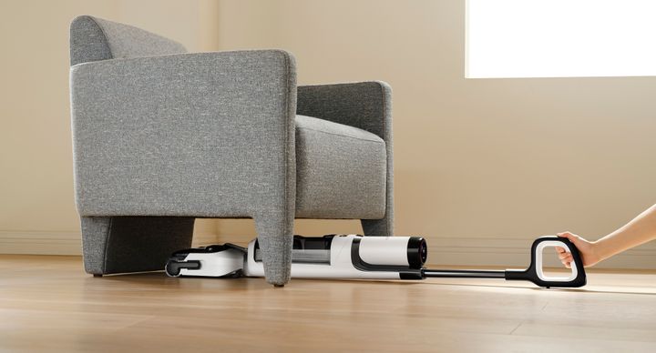 The Tineco vacuum being used in the lay-flat position to clean under an armchair