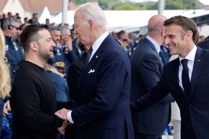 TOPSHOT - US President Joe Biden (C) shakes hands with Ukraine's President Volodymyr Zelensky (L) as France's President Emmanuel Macron (R) looks on during the International commemorative ceremony at Omaha Beach marking the 80th anniversary of the World War II 