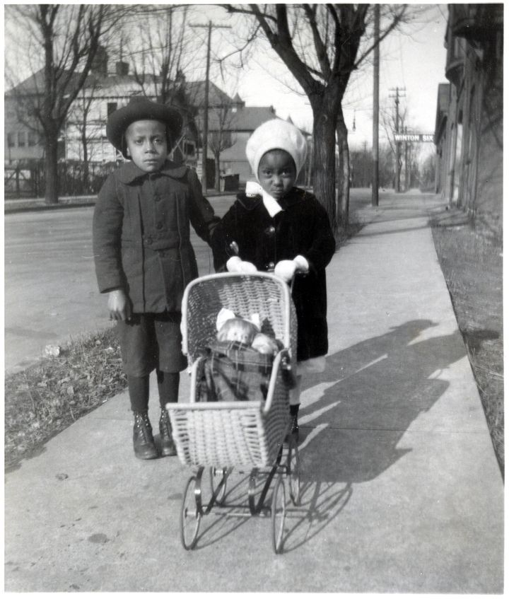 Two Black children push a white doll in a toy baby carriage down the sidewalk in the Walnut Hills neighborhood of Cincinnati, Ohio, in 1921.