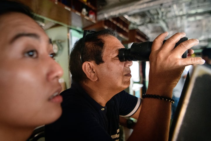 A ship captain named Jorge Dela Cruz, pictured at right on Dec. 10, 2023, in Palawan, Philippines, looks for Chinese vessels after turning his boat back from a civilian-led resupply mission to people on a contested group of islands due to the presence of Chinese navy and coast guard ships in the area.