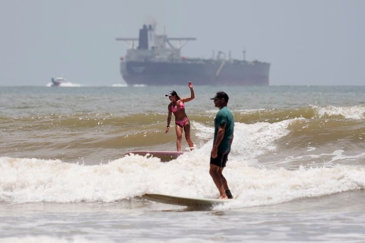 Ein Öltanker fährt ins offene Wasser, während Surfer die Wellen ausnutzen, bevor Hurrikan Beryl am Samstag, den 6. Juli 2024 Port Aransas, Texas, trifft. (AP Photo/Eric Gay)