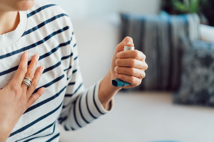 Woman using an asthma inhaler indoors. Using medication during an asthma attack