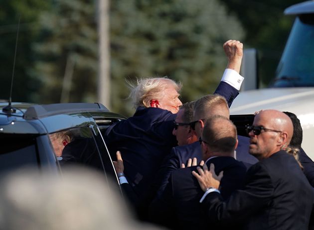 Trump raises his fist as he's helped into a vehicle.