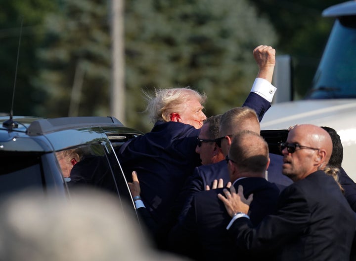 Trump raises his fist as he's helped into a vehicle.