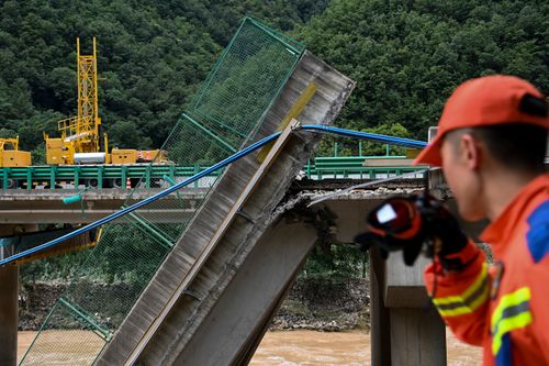 In this photo released by Xinhua News Agency, a rescuer looks at the collapsed bridge as they conduct a search and rescue on a river in Zhashui County in Shangluo City, northwest China's Shaanxi Province, Saturday, July 20, 2024.