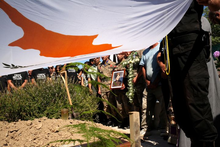 LARNACA, CYPRUS - 2014/10/04: Soldiers fold the Cyprus Flag in the cemetery, before placing the bones of Antoniadis Andreas Chrysanthos ( holding photograph ) in the grave. Funeral of Antoniadis Andreas Chrysanthos who was missing since the war in Cyprus after the Turkish invasion in 1974. Funeral and burial happened in Larnaca. (Photo by Yiorgos Doukanaris/Pacific Press/LightRocket via Getty Images)