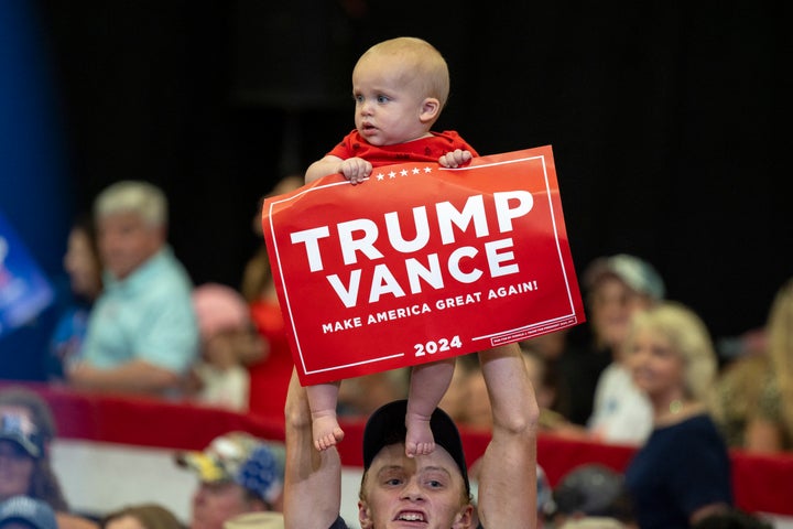 A man lifts a baby holding a "Trump Vance" sign at a rally for Republican vice presidential nominee JD Vance inside Radford University's Dedmon Center in Radford, Virginia, on July 22, 2024.