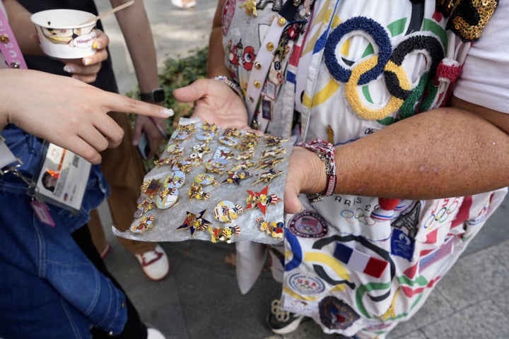 Vivianne Robinson lets a passer by choose one of the pins Robinson collected from USA Olympics 1984, during 2024 Summer Olympics, in Paris, France, Tuesday, July 30, 2024. The Olympics superfan has attended seven Games over the span of 40 years. (AP Photo/Lujain Jo)