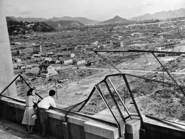 原爆投下後3年目の1948年に撮影された広島の町。一面の焼け野原にもぼつぼつ家が建てられている。ビルの屋上から2人連れが町を見下ろしている