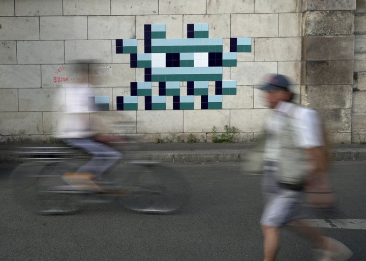 Um ciclista pedala em frente a um novo mosaico com tema olímpico feito misteriosamente às margens do Rio Sena pelo artista de rua francês conhecido apenas pelo nome de Invasor.
