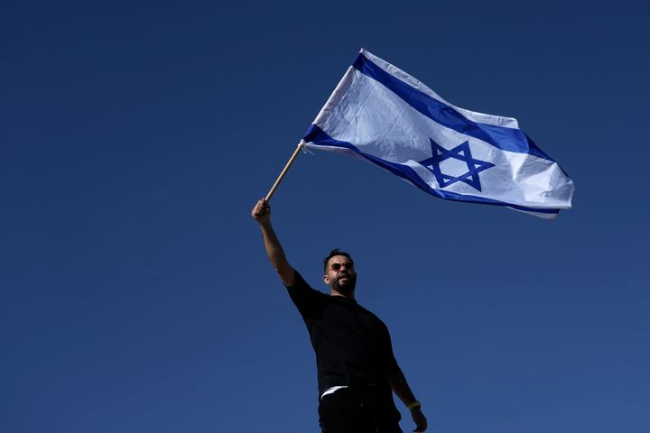 A protester waves the Israeli national flag in support of soldiers being questioned for detainee abuse, outside of the Sde Teiman military base, Monday, July 29, 2024. 