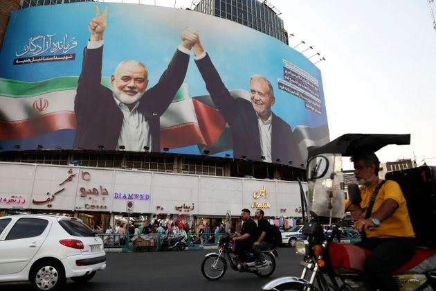 Vehicles drive past a huge banner showing the late Hamas leader Ismail Haniyeh, left, who was killed in an assassination last week, joining hands with Iranian President Masoud Pezeshkian, in a square in downtown Tehran, Iran, Monday, Aug. 5, 2024. Iran has vowed to respond with 